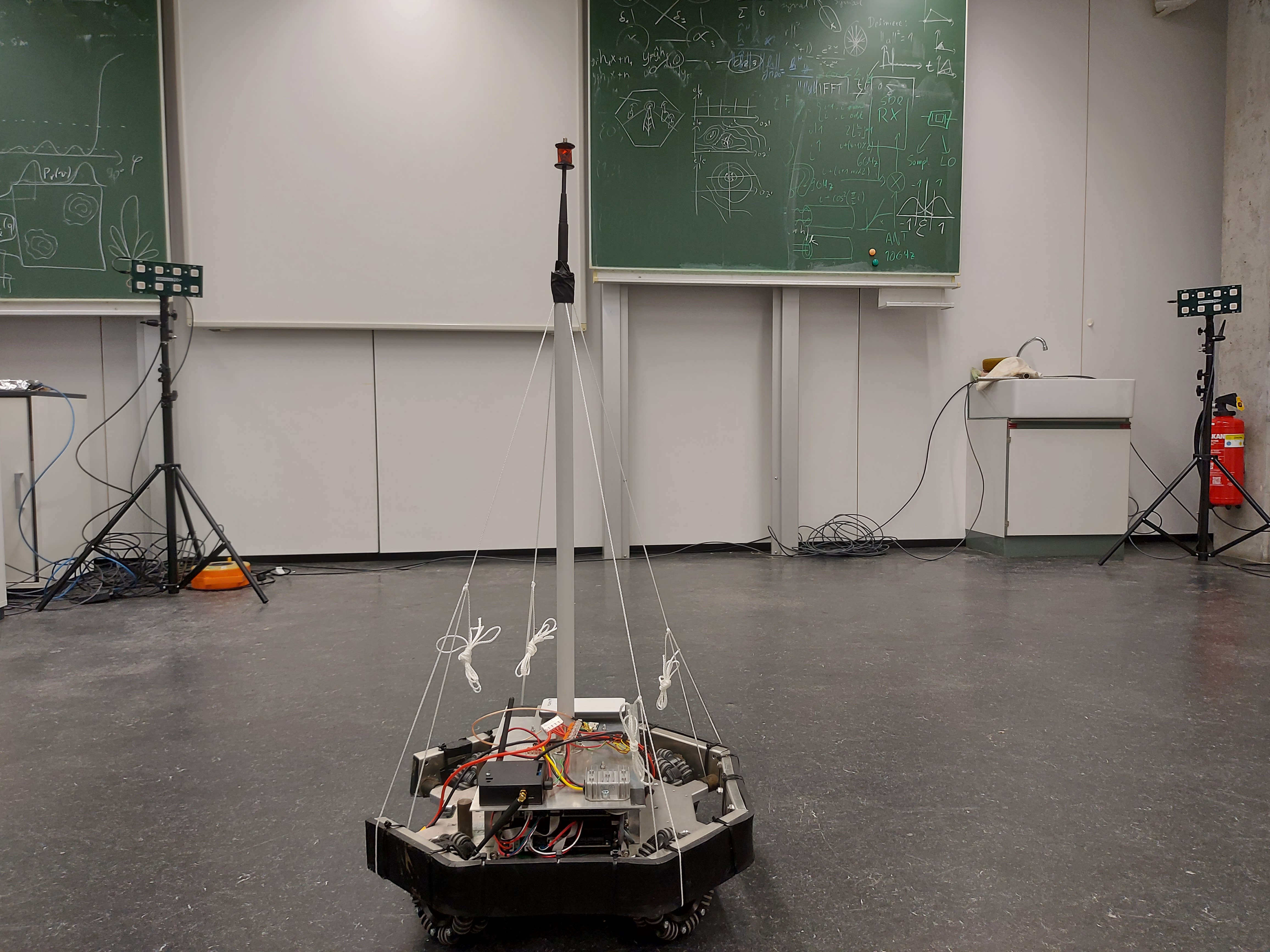 Robot with antenna and prism for tracking, and two ESPARGOS arrays in the background.